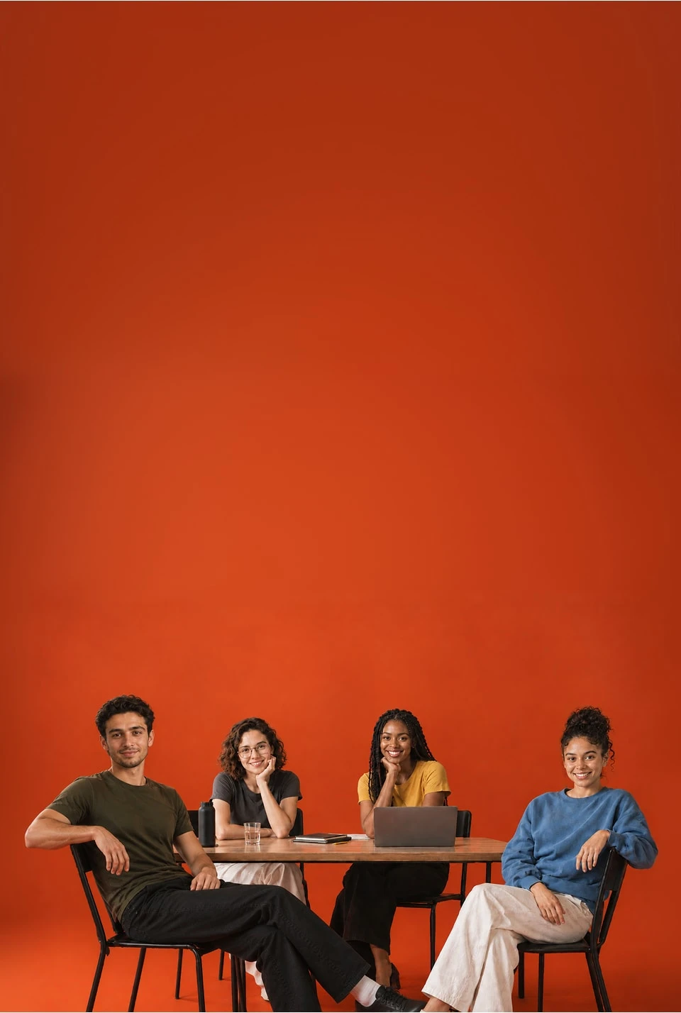 Four smiling team members at a table with a laptop in front of a vermilion wall